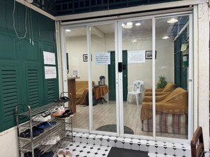A hotel entrance with a shoe rack, a waiting area with a sofa and chairs, and a closed door with a safety warning sign. - Atlas Hostel Khaosan (Bangkok)