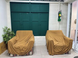 Two covered chairs in front of a green door, a potted plant to the left, and a fire extinguisher mounted on the wall. - Atlas Hostel Khaosan (Bangkok)