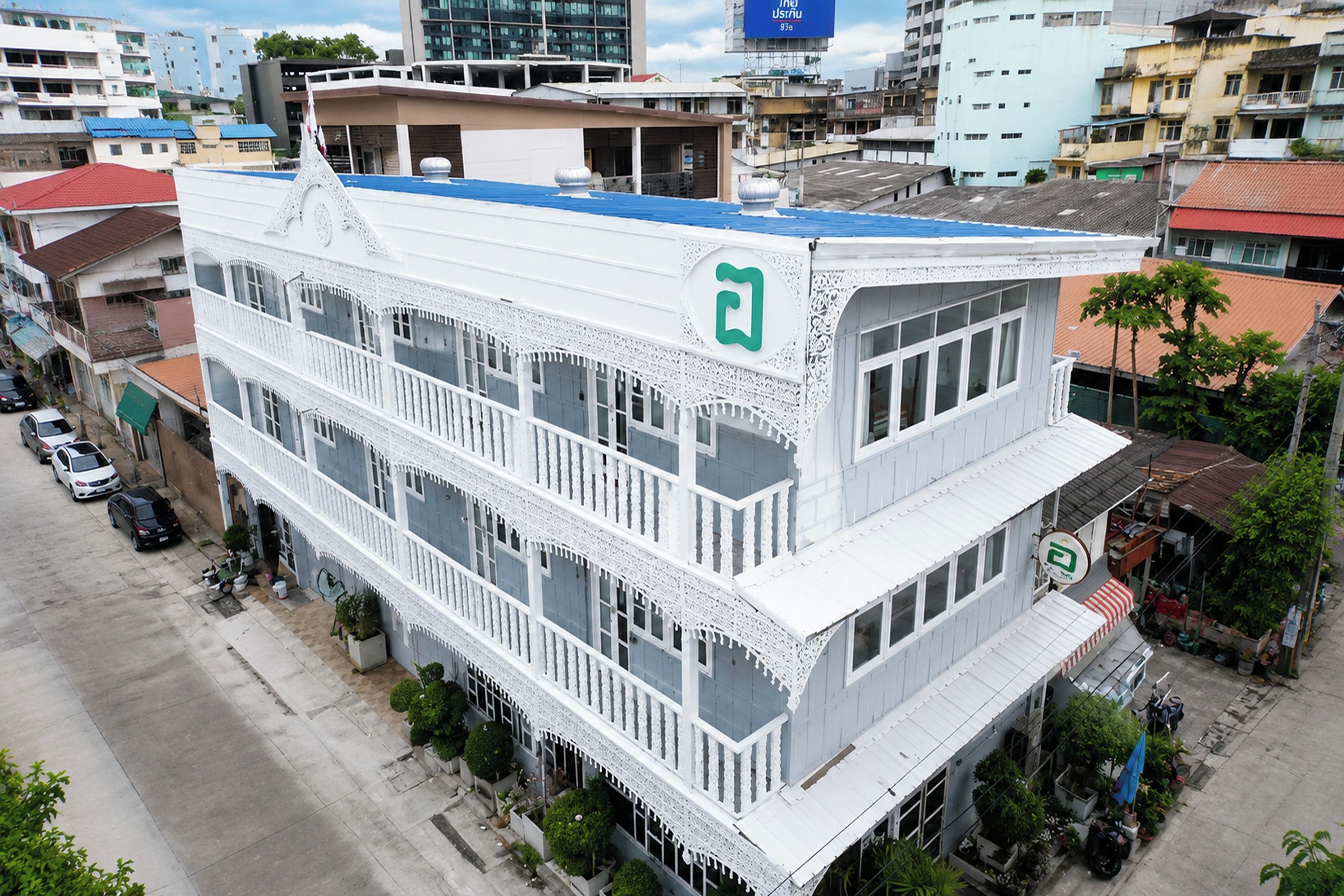 A multi-story building with a white facade, balconies, and a green logo on the top floor.