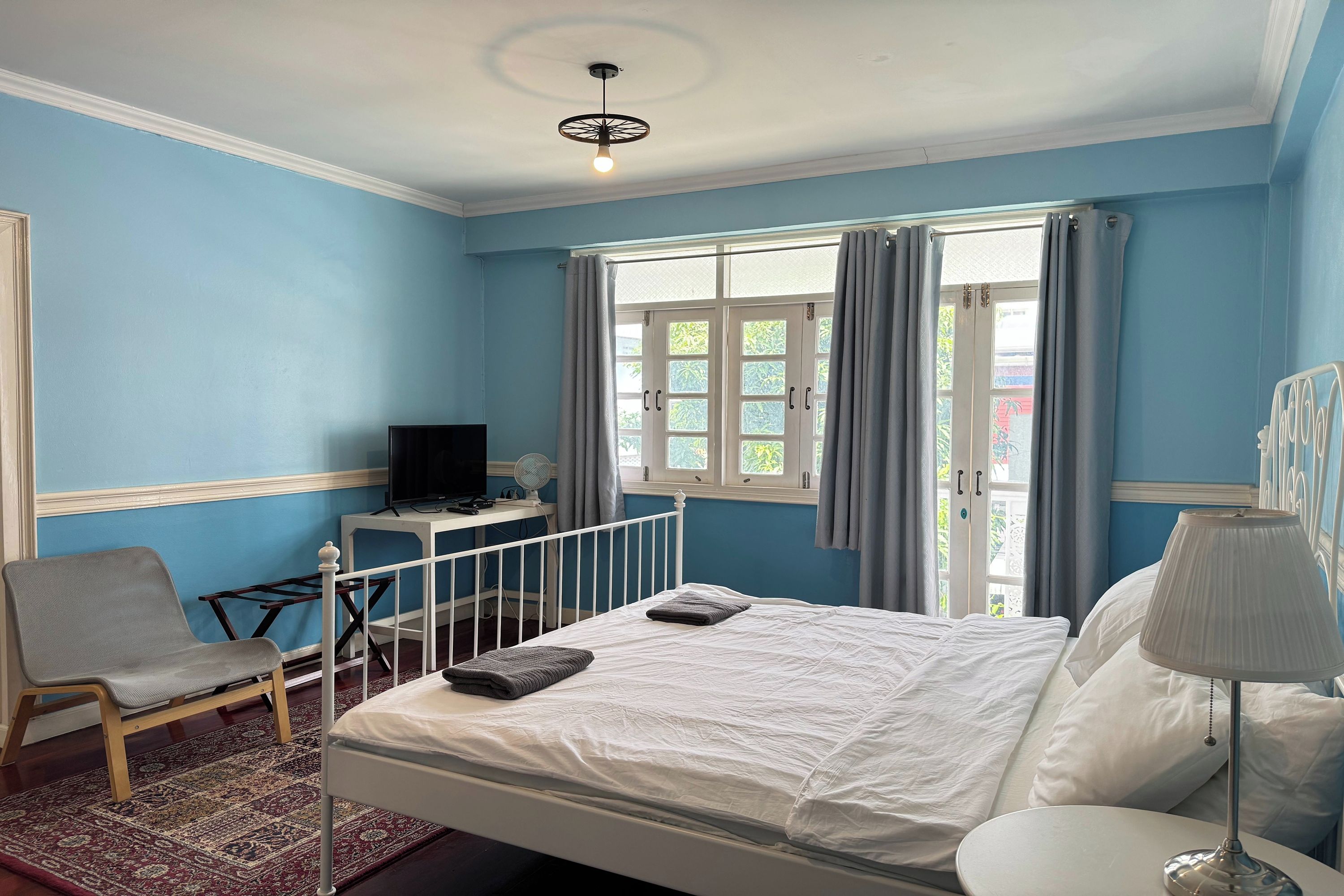 A bedroom with a bed, a chair, a desk with a television, and a window with curtains.