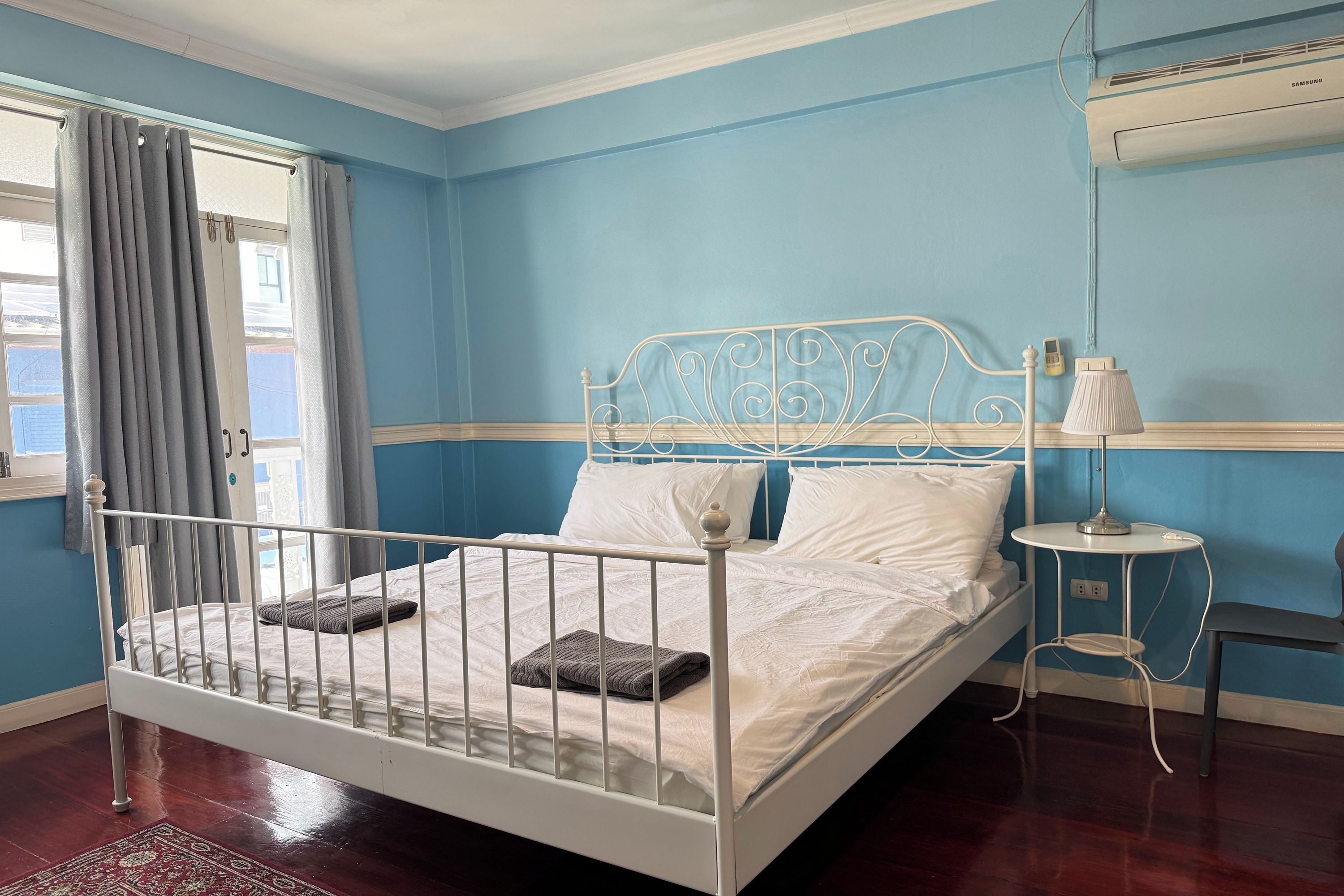 Una habitación con una cama individual, una mesita de noche con lámpara y una ventana con cortinas.
