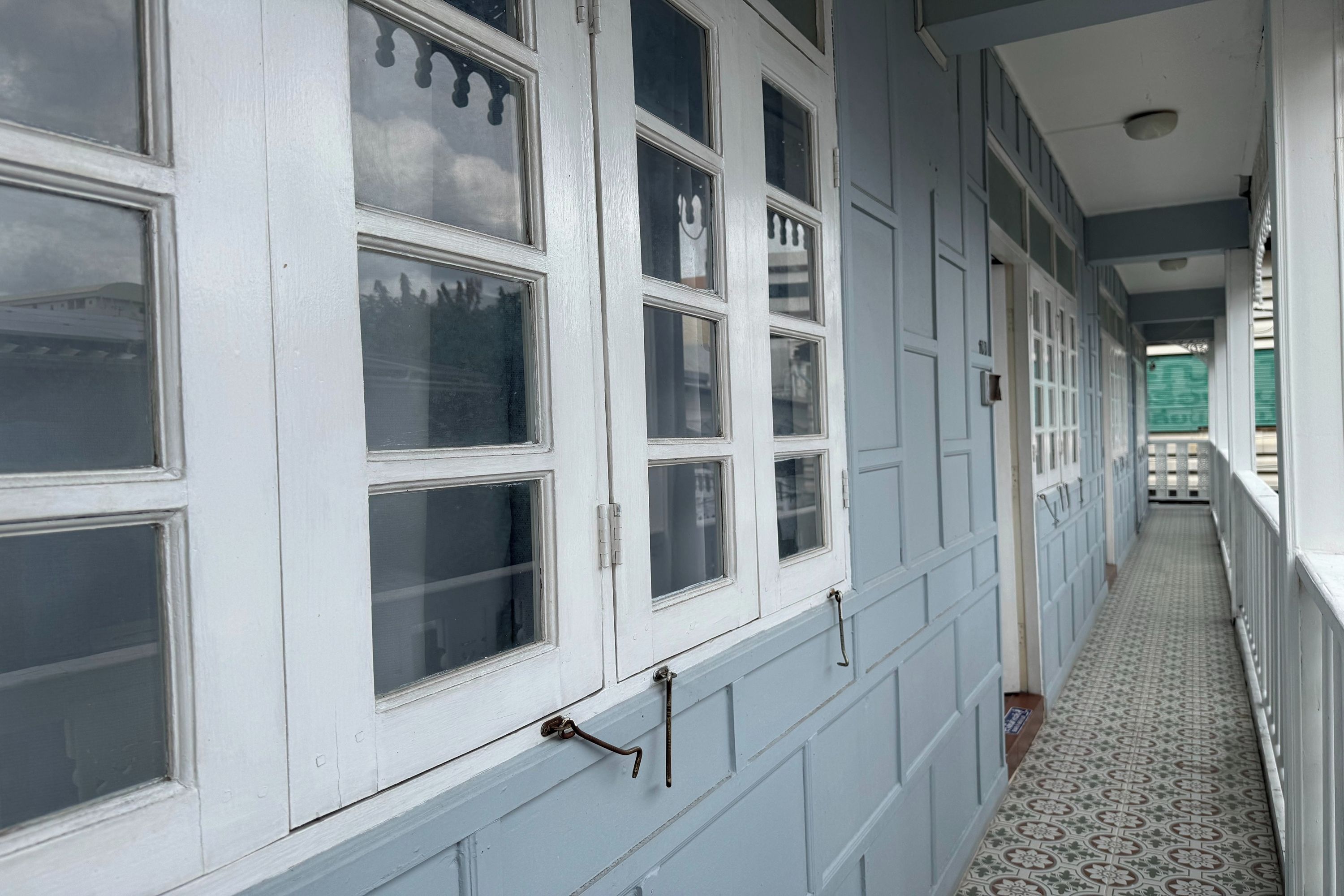 A corridor with multiple windows and doors, a patterned floor, and a view of a green vehicle outside.