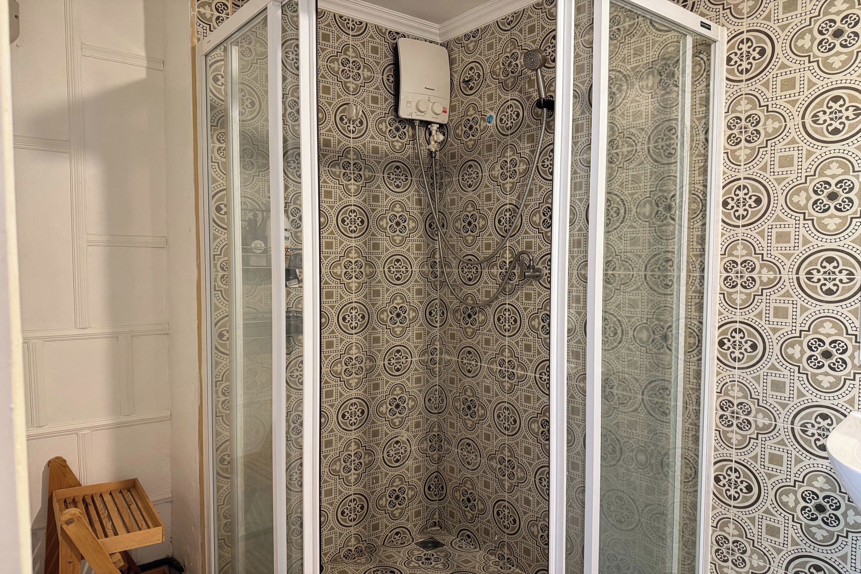 A shower with a patterned wall and a wooden chair.
