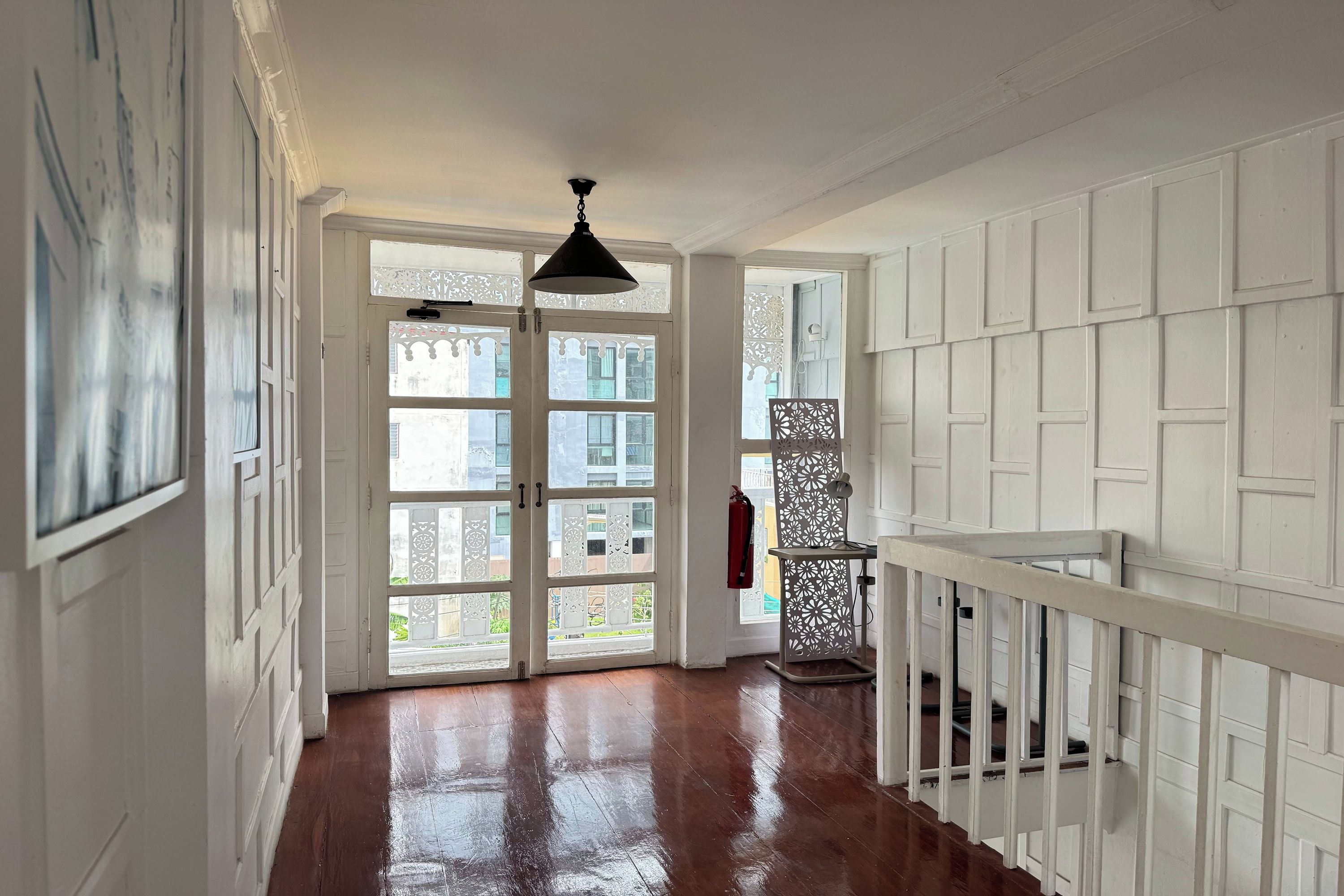 A hallway with a wooden floor, white walls, and a black pendant light.