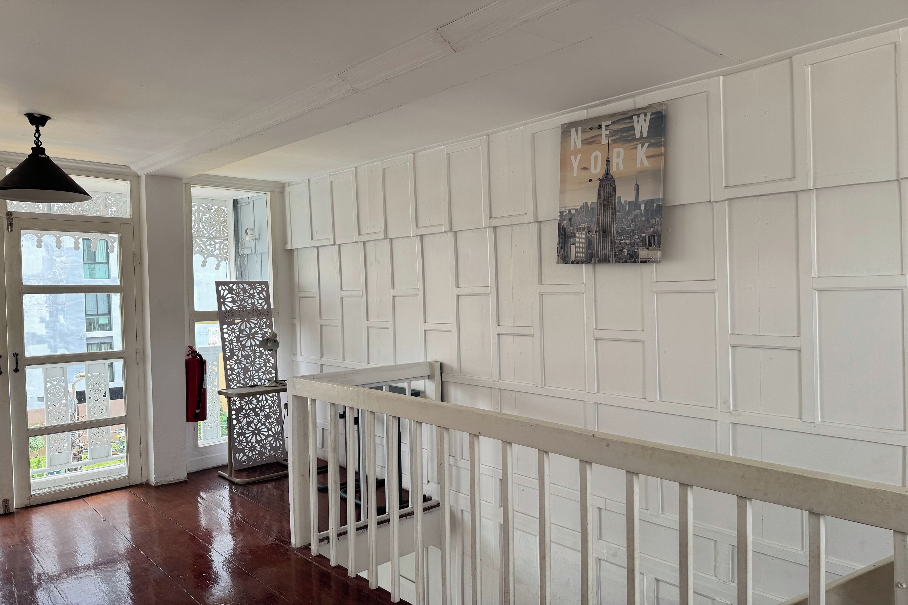 A hallway with white paneling, a staircase with a white railing, and a cityscape artwork on the wall.