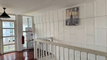 A hallway with white paneling, a staircase with a white railing, and a cityscape artwork on the wall.
