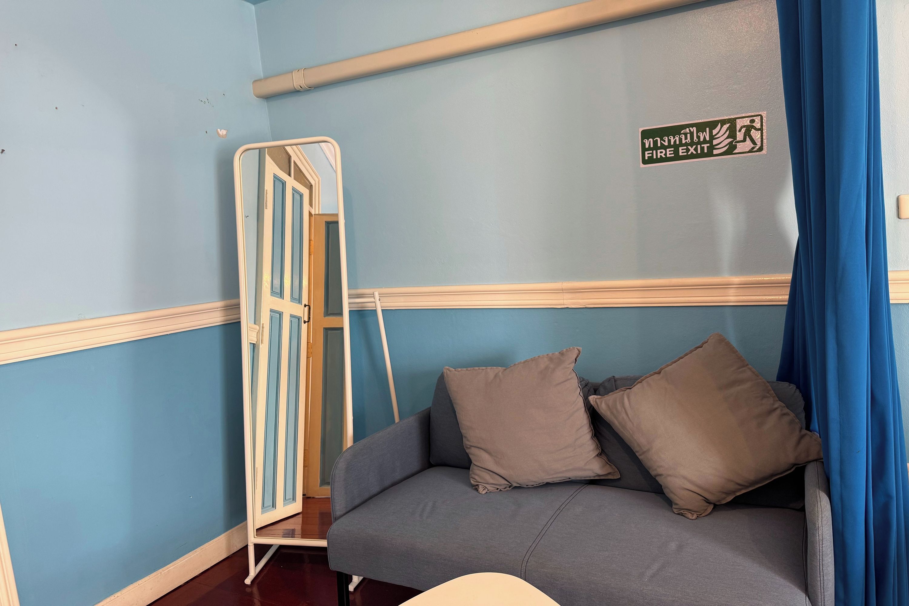 Una habitación con pared azul, un sofá gris con dos almohadas, un marco de puerta blanco y un letrero de salida de incendios.