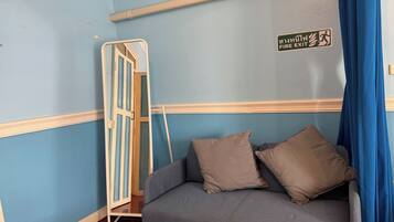 Una habitación con pared azul, un sofá gris con dos almohadas, un marco de puerta blanco y un letrero de salida de incendios.
