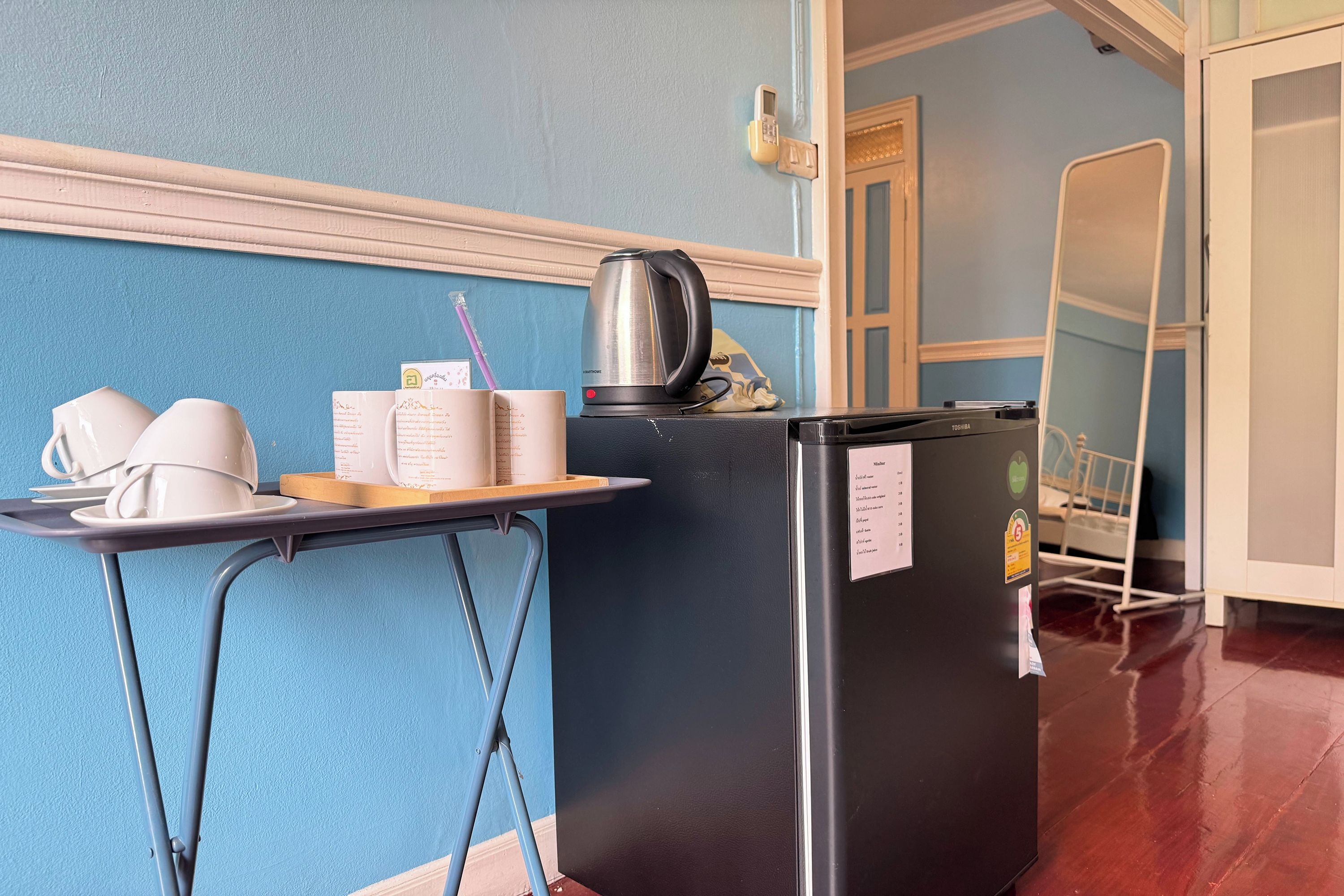 A kitchenette with a refrigerator, a kettle, and a tray with cups and a notebook.