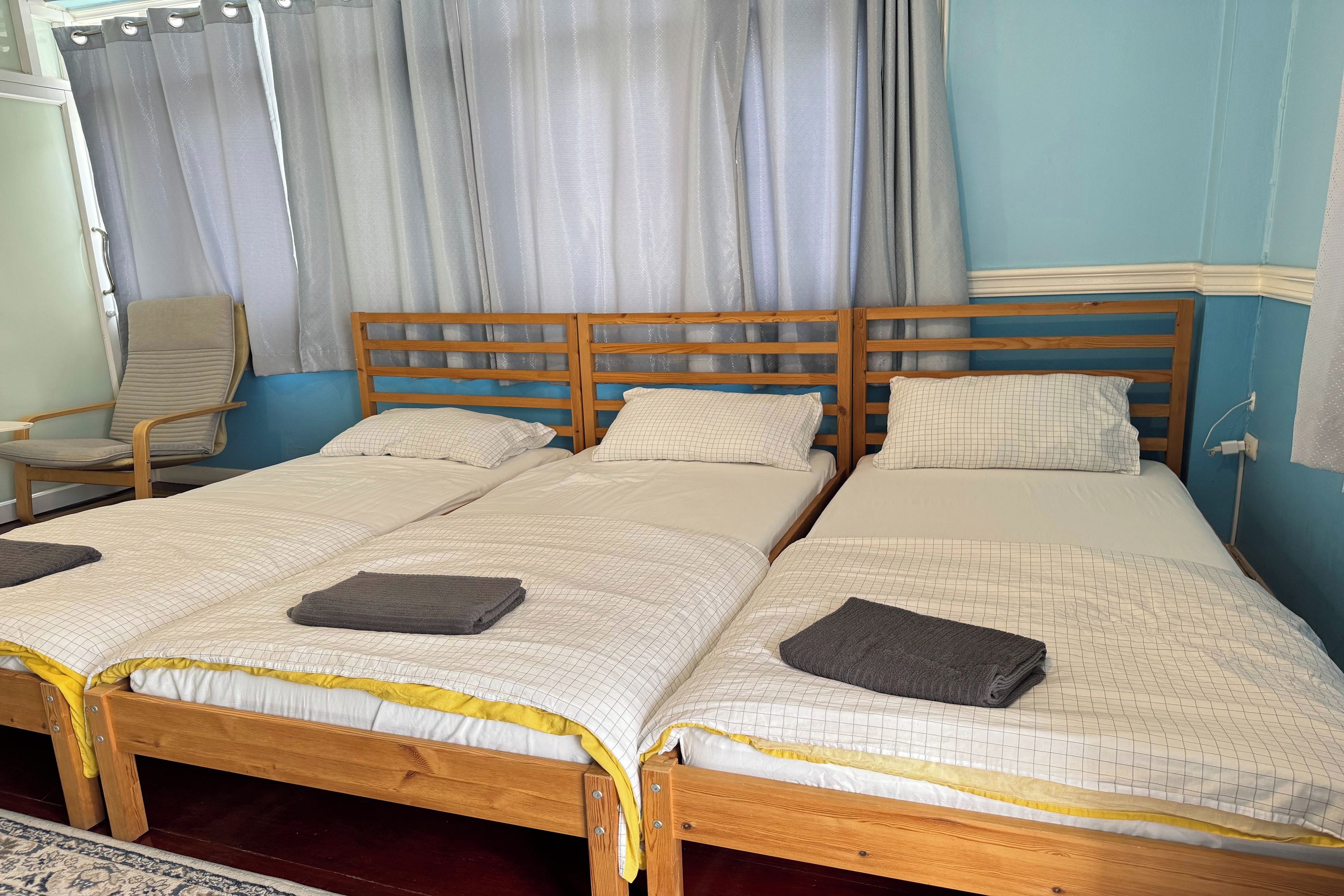 Una habitación con tres camas de madera, una silla y un ventanal con cortinas.