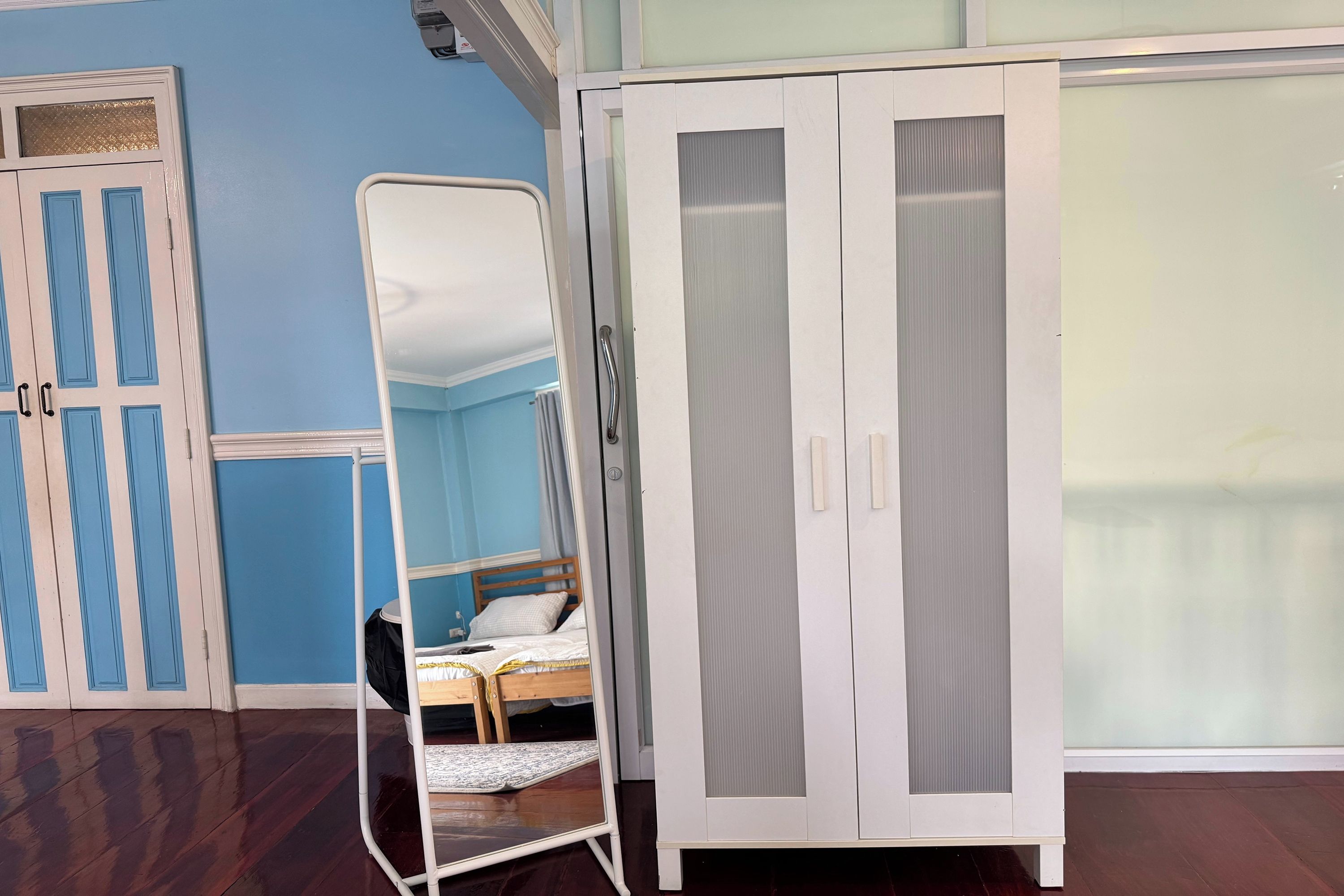 A room with a bed, a wardrobe, and a mirror stand.