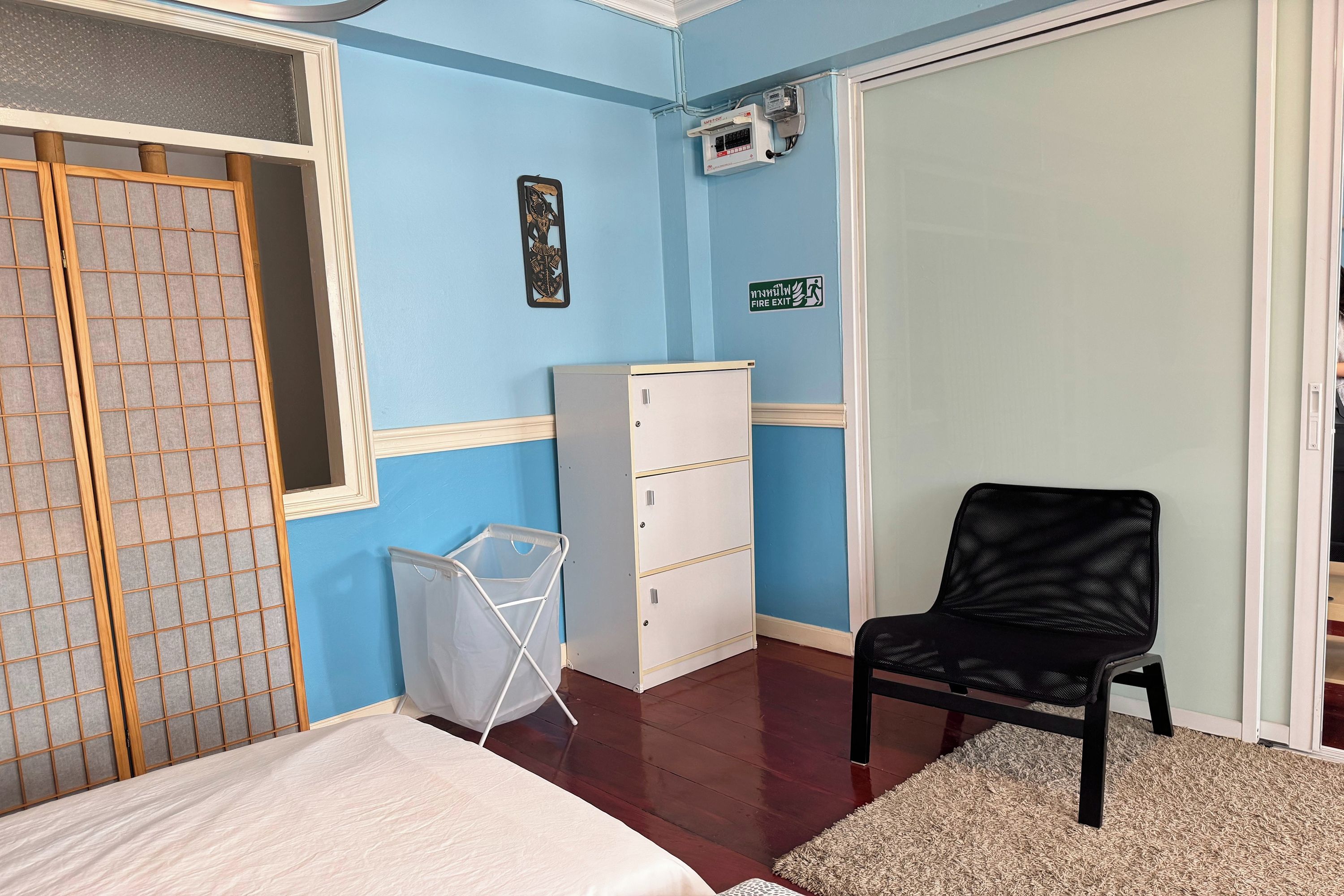A room with a bed, a chair, a white cabinet, a fire exit sign, and a window with a view.