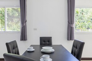 A dining area with a table, chairs, and a view of greenery through the windows. - Villa Ras Kamala (Kamala)