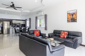 A modern living room with a black leather sofa, a glass coffee table, and a dining area with a black table and chairs. - Villa Ras Kamala (Kamala)