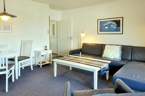 Ein Wohnzimmer mit einer Couch, einem Couchtisch, einem Esstisch mit Stühlen, einer Lampe und einer Tür.