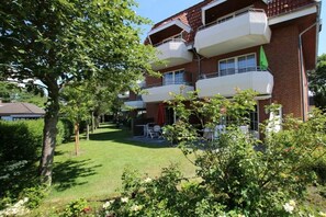 A multi-story residential building with balconies, a grassy yard, and outdoor furniture. - Holiday apartment with 1 bedroom (Wyk auf Föhr)