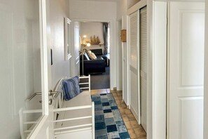 Ein schmaler Gang führt zu einem Schlafzimmer mit einem Bett, einem Nachttisch und einer Kommode.