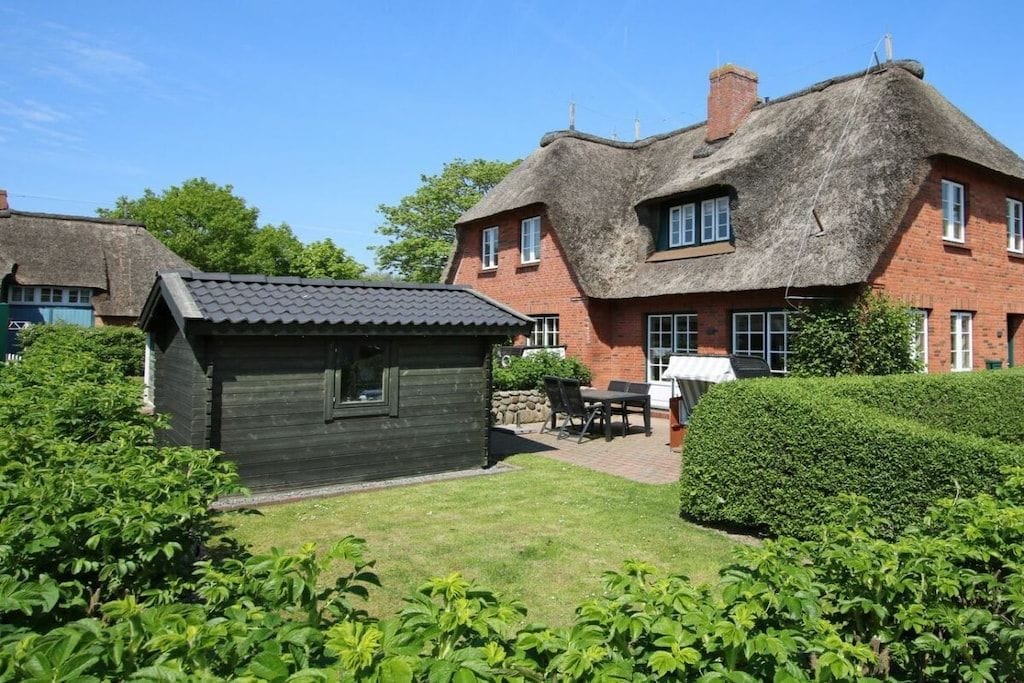 A traditional thatched-roof house with a small wooden structure in the foreground, surrounded by well-maintained greenery.