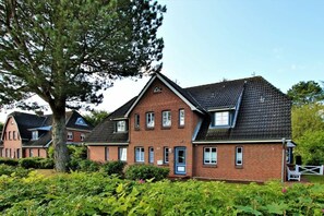 A two-story brick house with a gabled roof, a front porch, and a well-maintained garden. - Holiday apartment in Föhr with 2 bedrooms (Wyk auf Föhr)