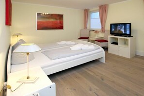 A hotel room with a bed, a television, a desk, and a window with curtains. - Holiday apartment in Föhr with 2 bedrooms (Wyk auf Föhr)