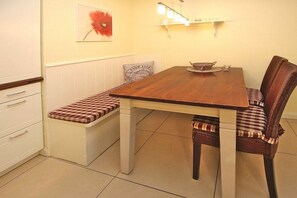 A dining area with a wooden table, bench seating, and a wall-mounted light fixture. - Holiday apartment in Föhr with 2 bedrooms (Wyk auf Föhr)