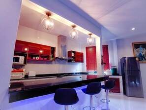 Una cuina moderna amb una illa central, tamborets d'esbarjo i armaris vermells.