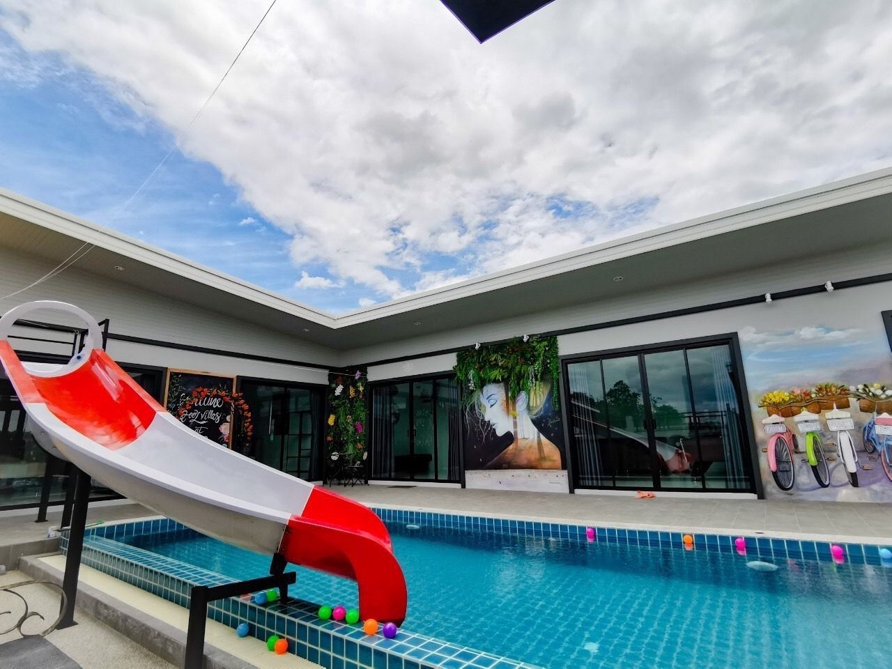 A swimming pool with a red and white slide, a mural, and a view of the sky.