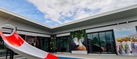 A swimming pool with a red and white slide, a mural, and a view of the sky.