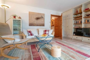 A living room with a sofa, a glass coffee table, a wicker ottoman, a bookshelf, and a television. - Holiday apartment with 1 bedroom (St.Peter-Ording)