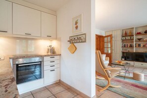 A modern kitchen with white cabinetry, a Bosch oven, and a dining area with a wooden chair and a television. - Holiday apartment with 1 bedroom (St.Peter-Ording)