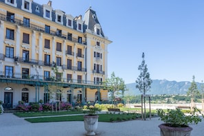 Un edificio a più piani con balconi, una zona giardino con piante in vaso e una vista sulle montagne sullo sfondo.