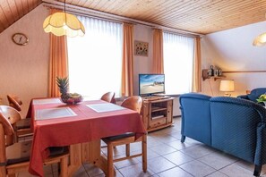 Ein Zimmer mit Esstisch, Stühlen, Fernseher, Sofa und Lampe.