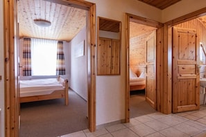 Quarto com teto de madeira, uma cama, janela com cortinas e porta que dá para outro espaço.
