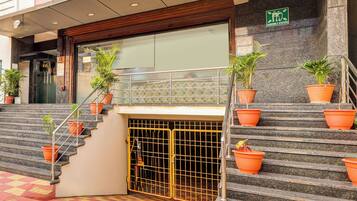 Entrada de hotel con escaleras, plantas en macetas y señalización de punto de encuentro de emergencia.