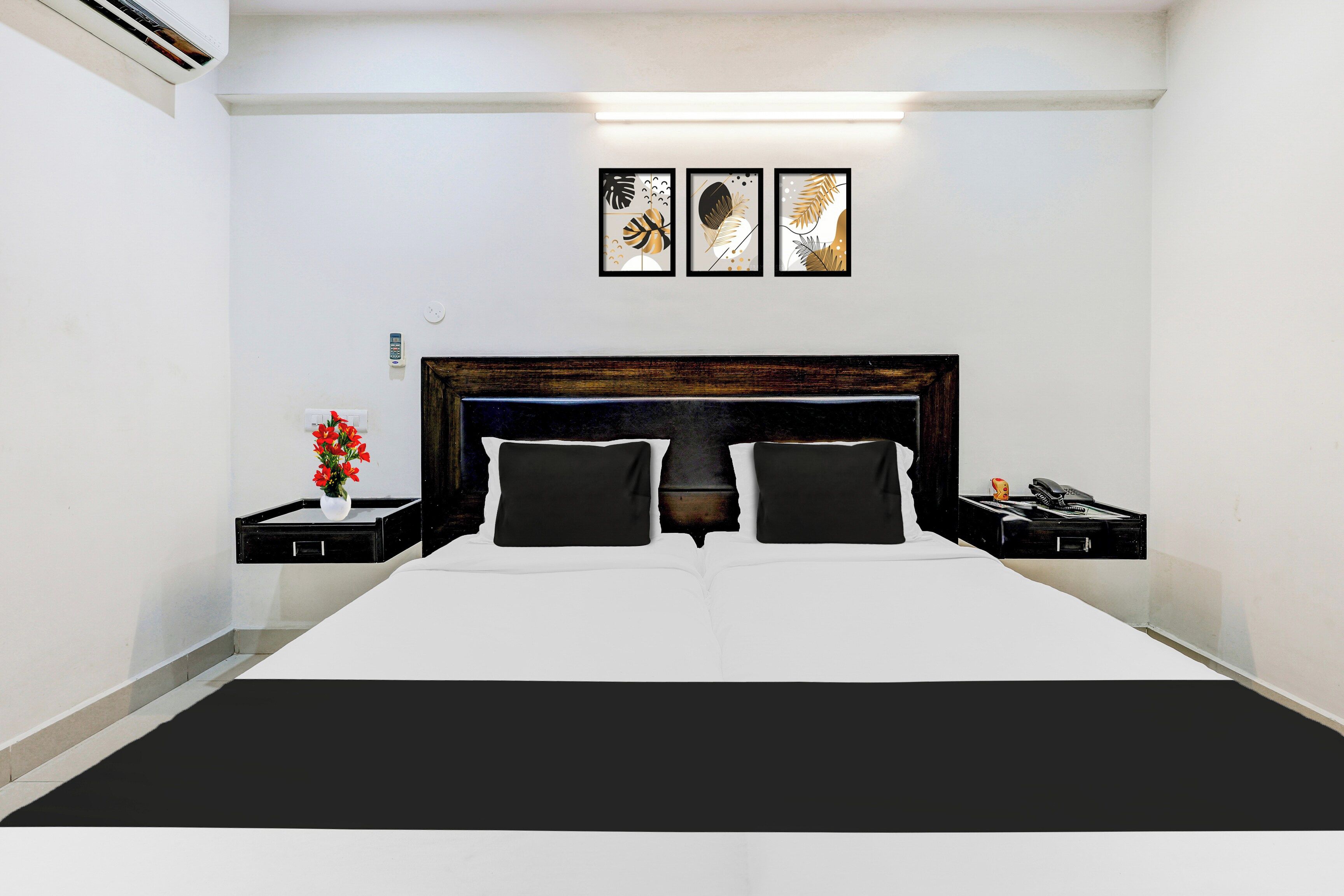 A hotel room with a large bed, two bedside tables, a nightstand, a wall-mounted phone, and three framed artworks above the bed.
