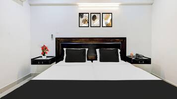 A hotel room with a large bed, two bedside tables, a nightstand, a wall-mounted phone, and three framed artworks above the bed.