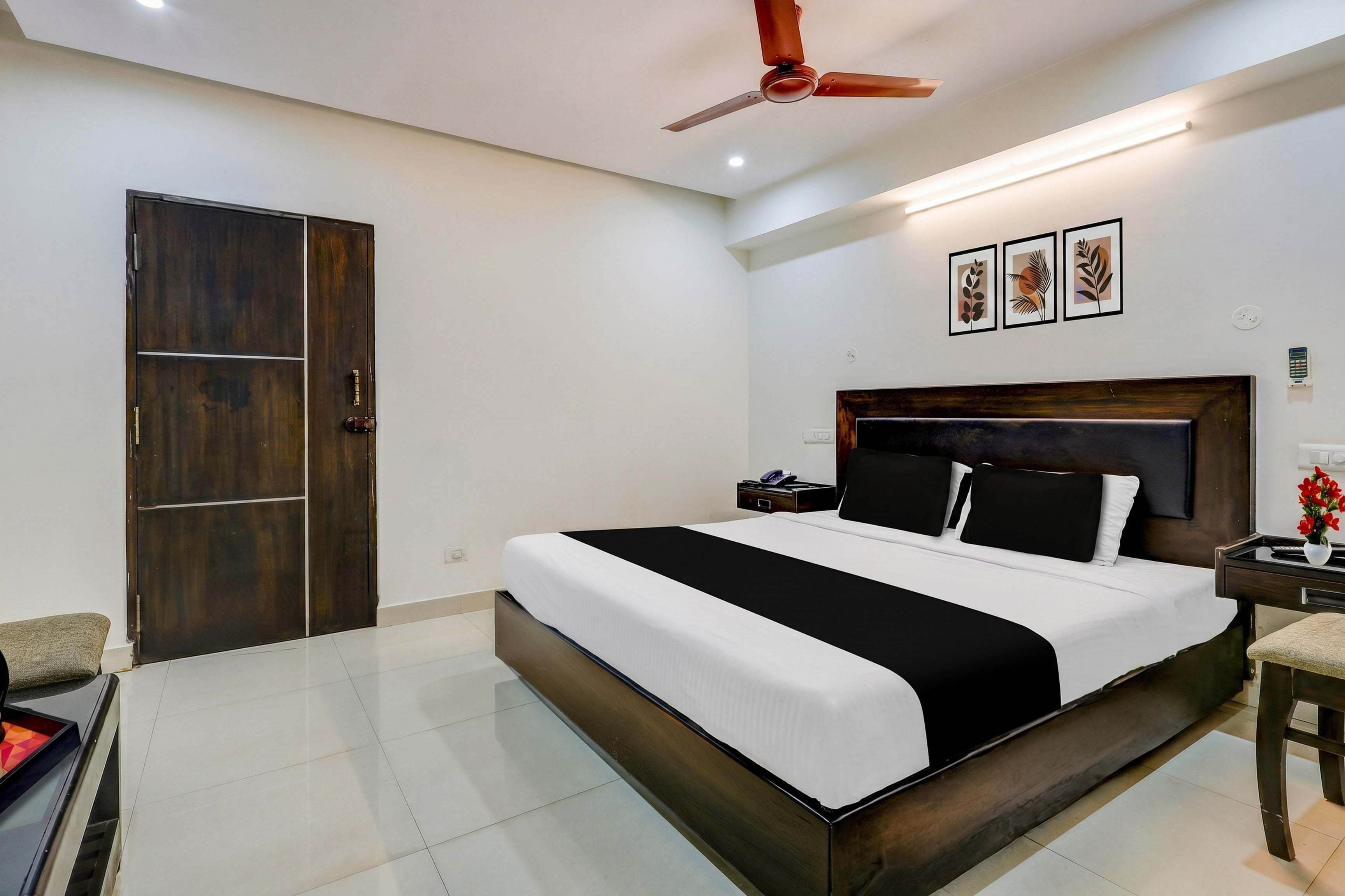 Una habitación de hotel con una cama grande, un armario de madera, un ventilador de techo y una mesita de noche con un teléfono.