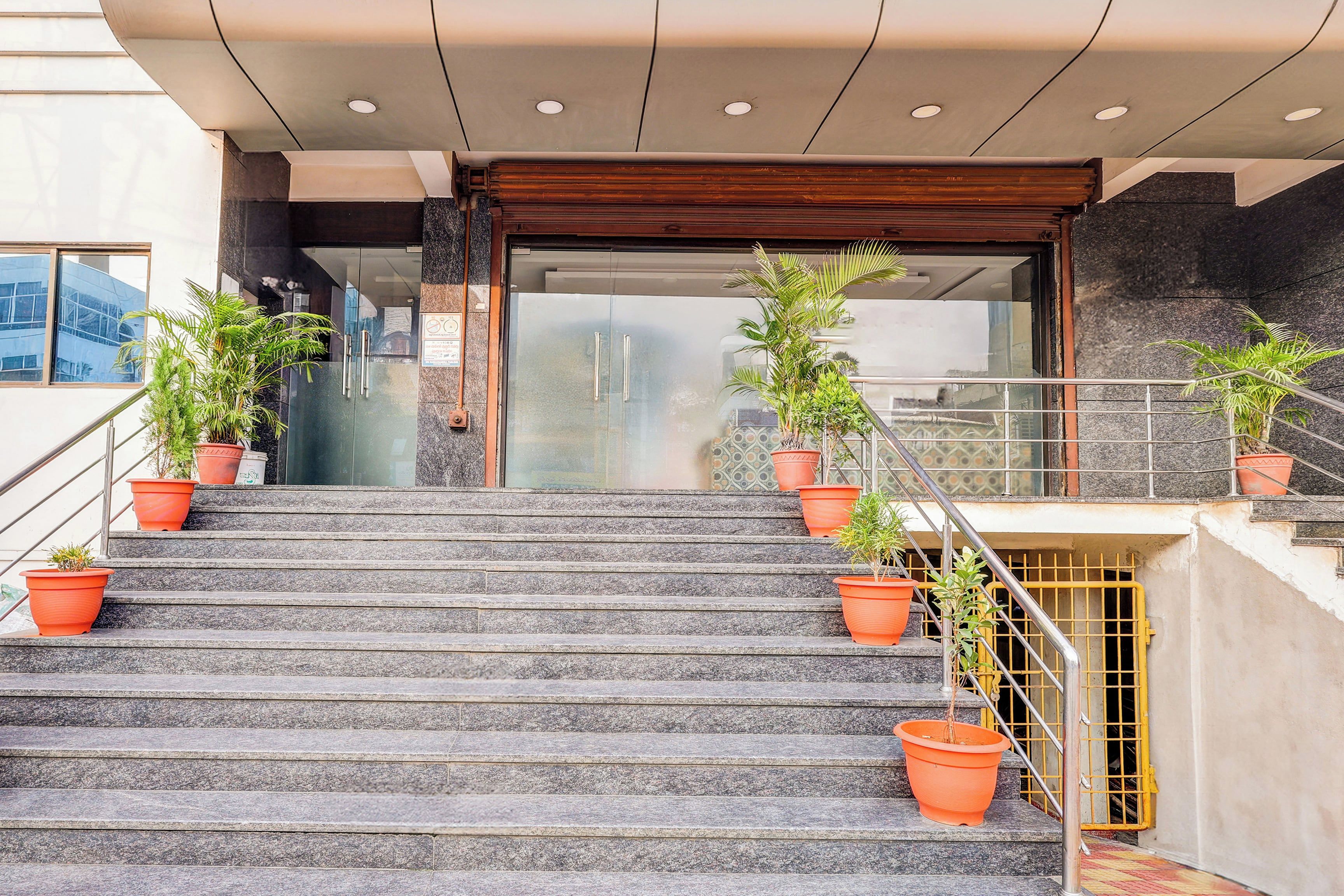 A set of stone steps leading to a building entrance with glass doors, flanked by potted plants.