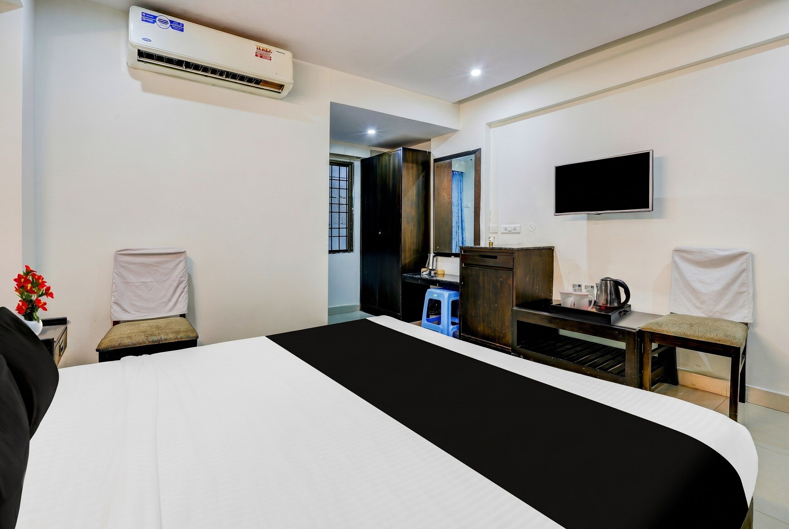 Habitación de hotel con cama, escritorio, silla, televisor y aire acondicionado.