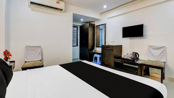 Habitación de hotel con cama, escritorio, silla, televisor y aire acondicionado.