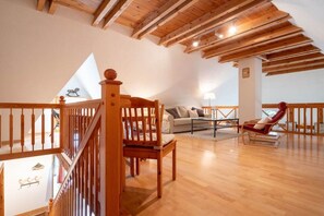 A spacious loft with wooden beams, a wooden staircase, a sofa, a chair, and a lamp. - Holiday home with 2 bedrooms (St. Peter - Ording)