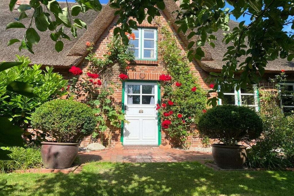 A traditional brick house with a thatched roof, a white door, and a small window above the door.