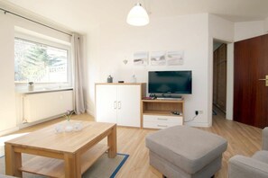 A modern living room with a wooden table, a sofa, a TV, and a cabinet. - Flurstraße 10, Holiday Apartment 1 (Wyk auf Föhr)
