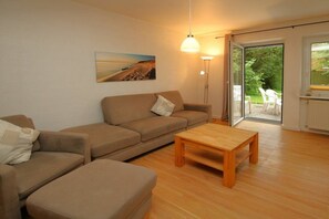 A living room with a sofa, a wooden coffee table, a floor lamp, and a painting on the wall. - Flurstraße 10, Holiday Apartment 1 (Wyk auf Föhr)