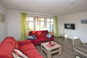 A living room with a red sofa, a wooden coffee table, and a television on the wall. - Strandstraße 18 b, Apt. 1, Haus Paula (Wyk)