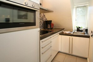 A compact kitchen with a built-in oven, a coffee maker, and a window providing natural light. - Lüttmarsch 13, Holiday Apartment 10 (Wyk auf Föhr)