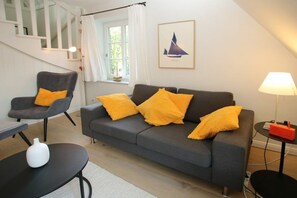 A living room with a grey sofa, two armchairs, a small table with a white vase, a lamp, and a framed picture on the wall. - Lüttmarsch 13, Holiday Apartment 10 (Wyk auf Föhr)