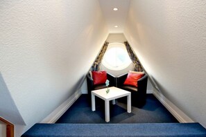 A small, narrow room with a white ceiling, a single white table, two black sofas with red cushions, and a window with curtains. - Rungholtstraße 6a, Holiday Apartment 3 (Wyk auf Föhr)