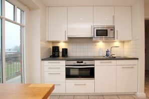 A modern kitchen with white cabinets, a microwave, an oven, and a coffee maker. - Rungholtstraße 6a, Holiday Apartment 3 (Wyk auf Föhr)