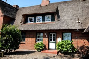 Ein traditionelles Backsteinhaus mit Strohdach, einer Haustür und einem kleinen Veranda-Bereich.